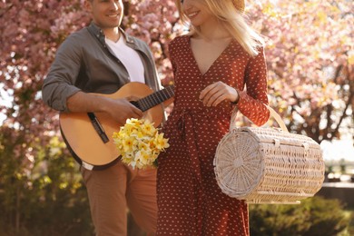 Photo of Lovely couple with picnic basket, flowers and guitar in park on sunny spring day, closeup