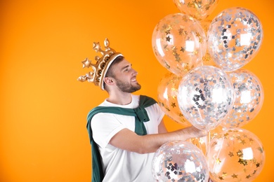 Young man with crown and air balloons on color background