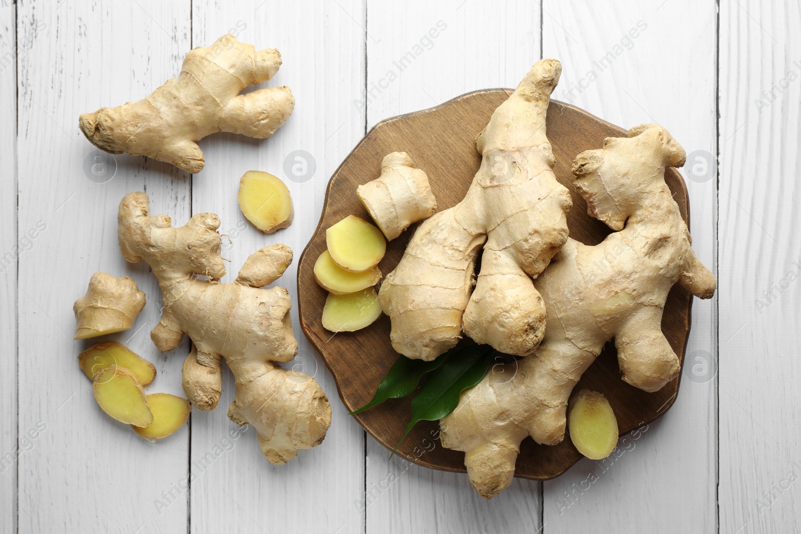 Photo of Cut and whole fresh ginger with leaves on white wooden table, flat lay