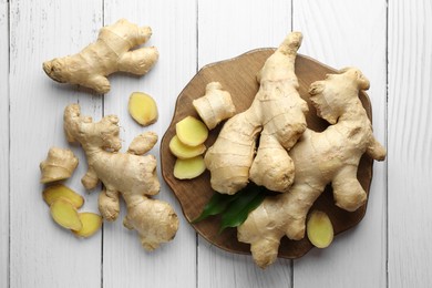 Photo of Cut and whole fresh ginger with leaves on white wooden table, flat lay