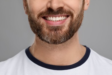 Smiling man with healthy clean teeth on grey background, closeup