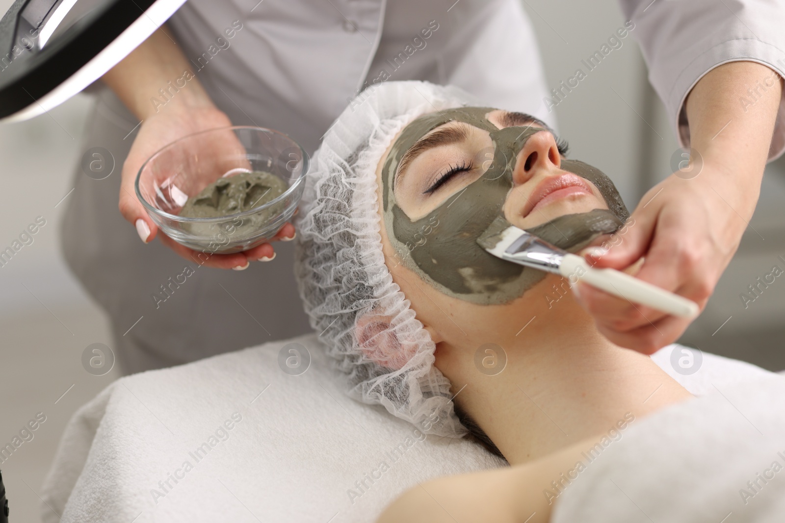 Photo of Cosmetologist applying mask on woman's face, closeup