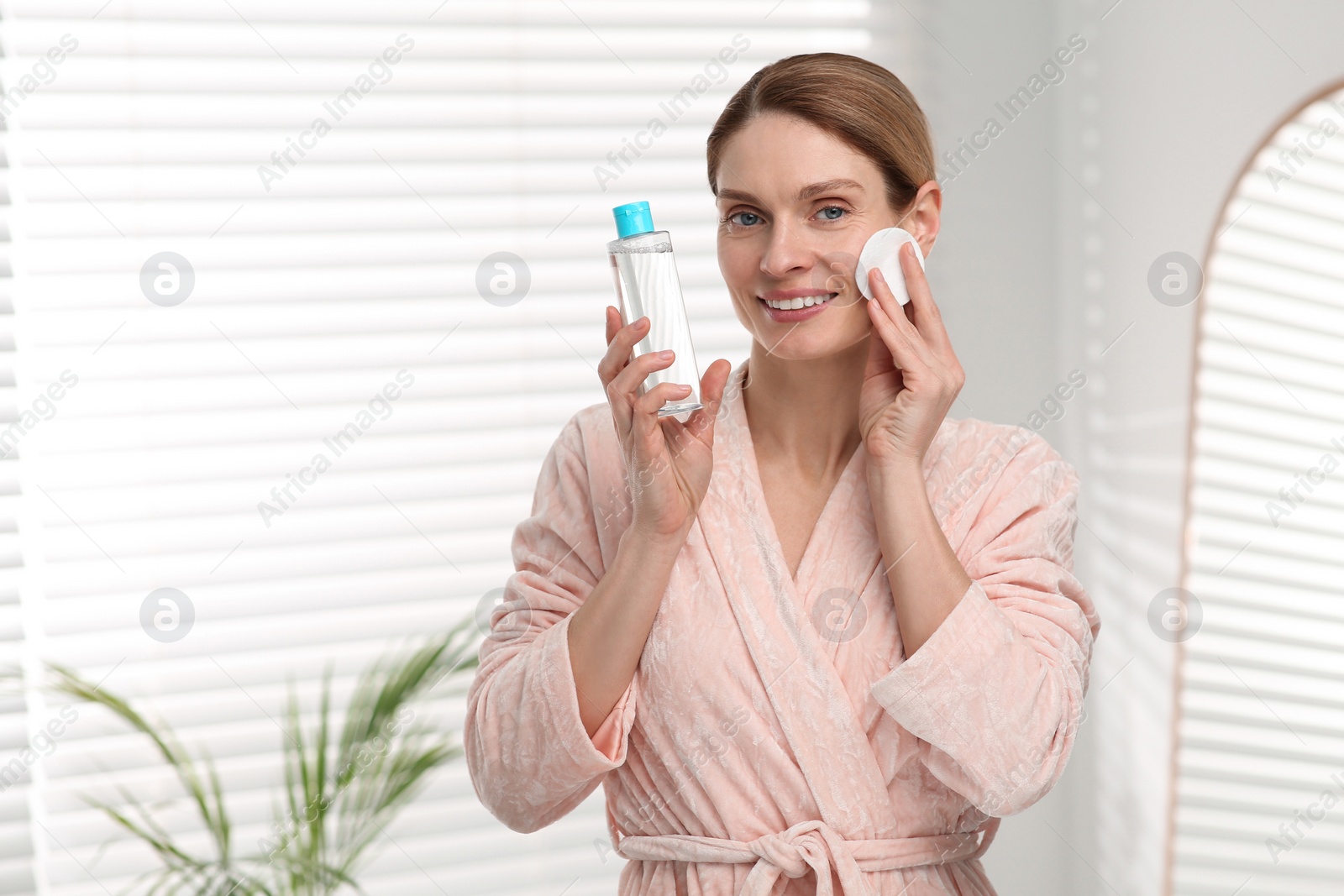 Photo of Beautiful woman removing makeup with cotton pad indoors