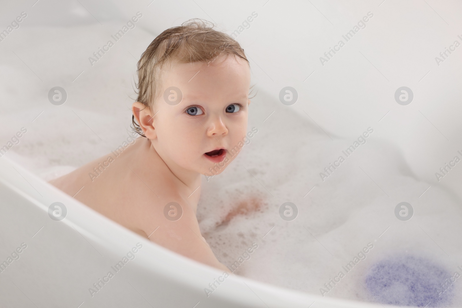 Photo of Cute little baby taking foamy bath at home