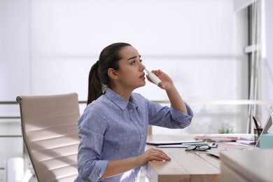 Photo of Sick young woman using nasal spray in office