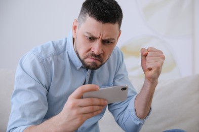 Photo of Emotional man with smartphone at home. Online hate concept