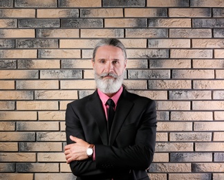 Handsome bearded mature man in suit near brick wall background