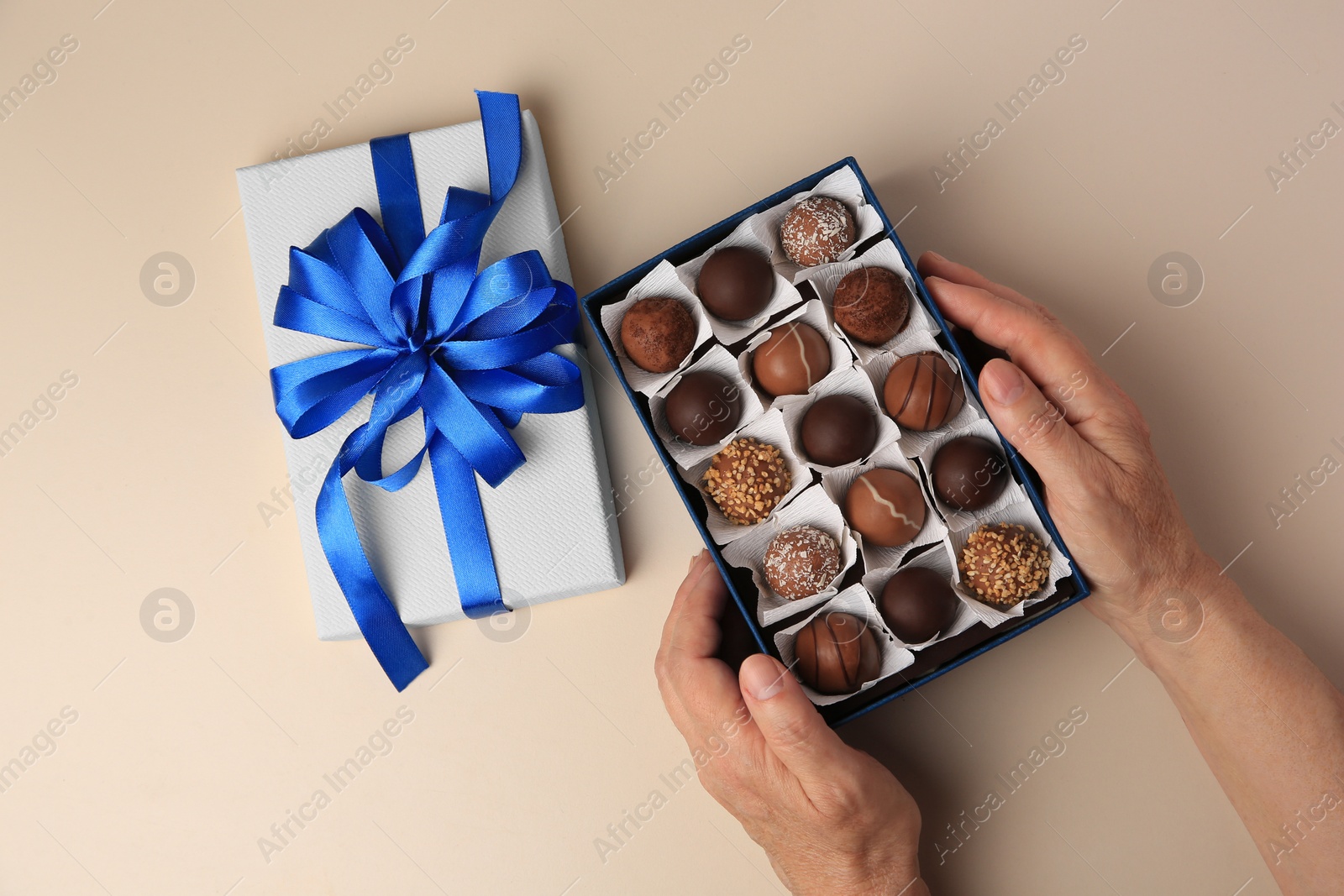 Photo of Woman with box of delicious chocolate candies on beige background, top view