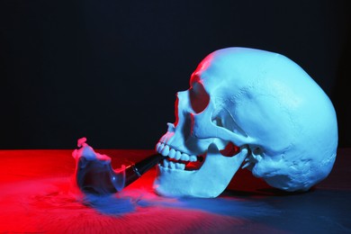 Human skull with pipe and smoke in neon lights on black background