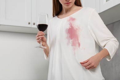 Photo of Woman with stain on her clothes and glass of wine indoors, closeup
