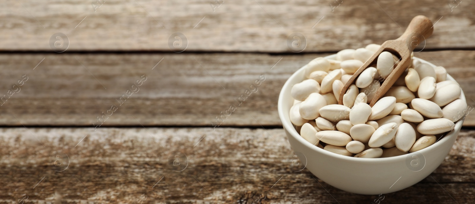 Image of Bowl and scoop with uncooked white beans on wooden table, space for text. Banner design