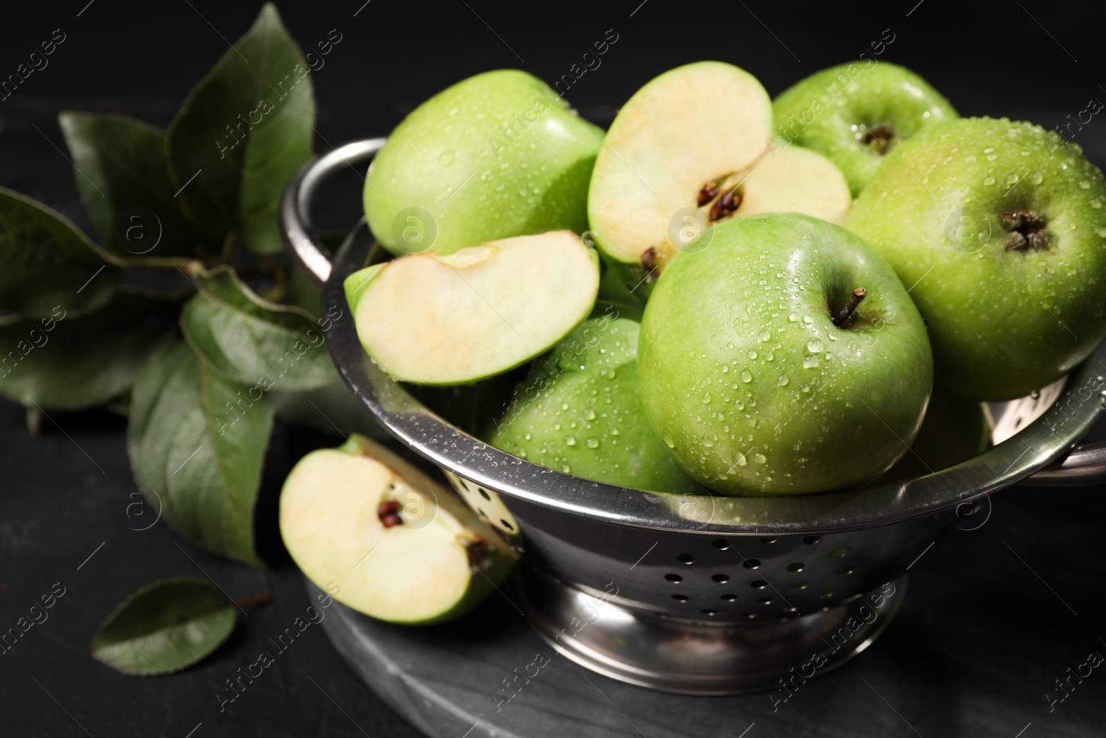 Photo of Ripe green apples with water drops and leaves on black table, closeup