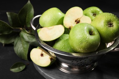 Photo of Ripe green apples with water drops and leaves on black table, closeup