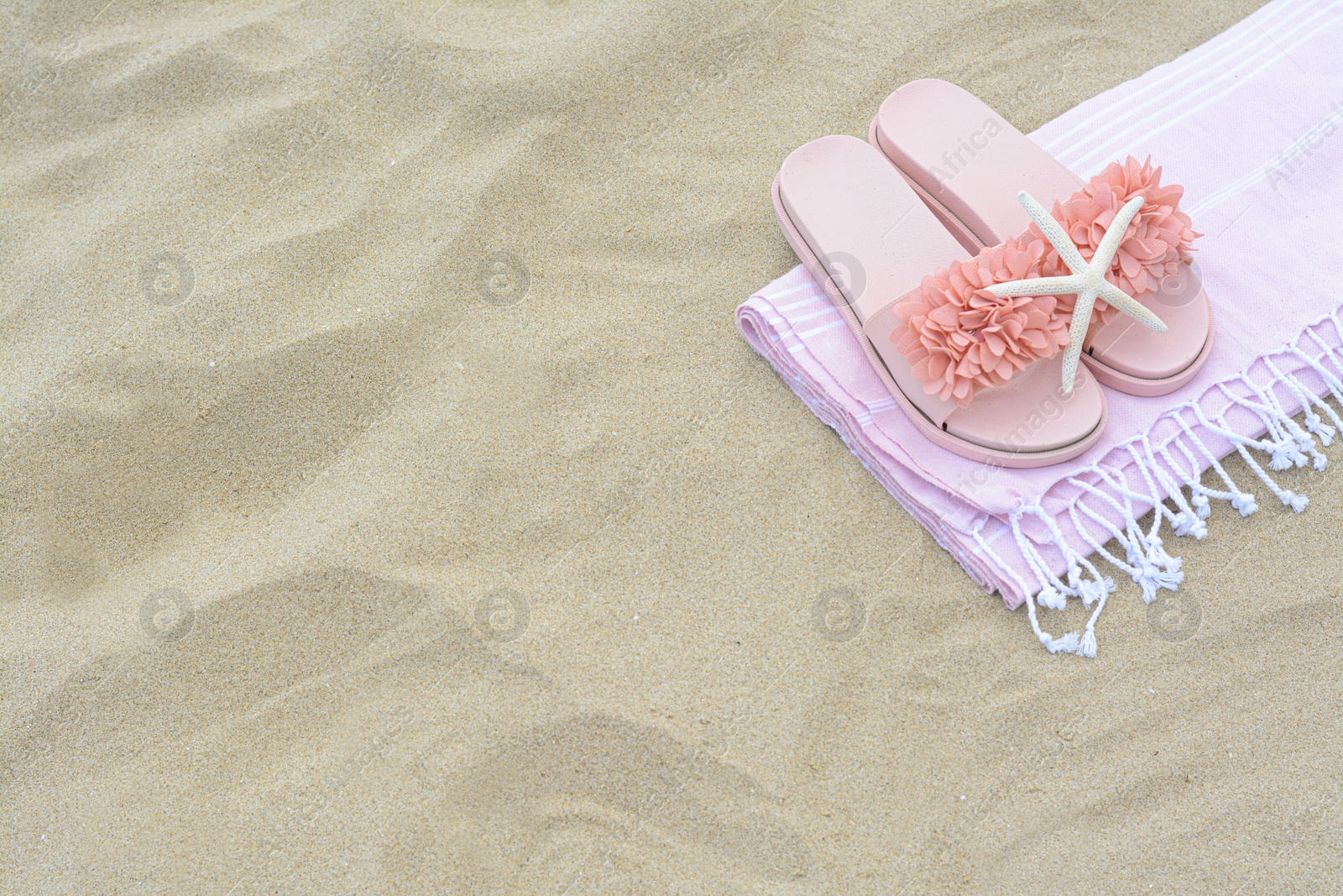 Photo of Blanket, stylish slippers and starfish on sand outdoors, above view with space for text. Beach accessories