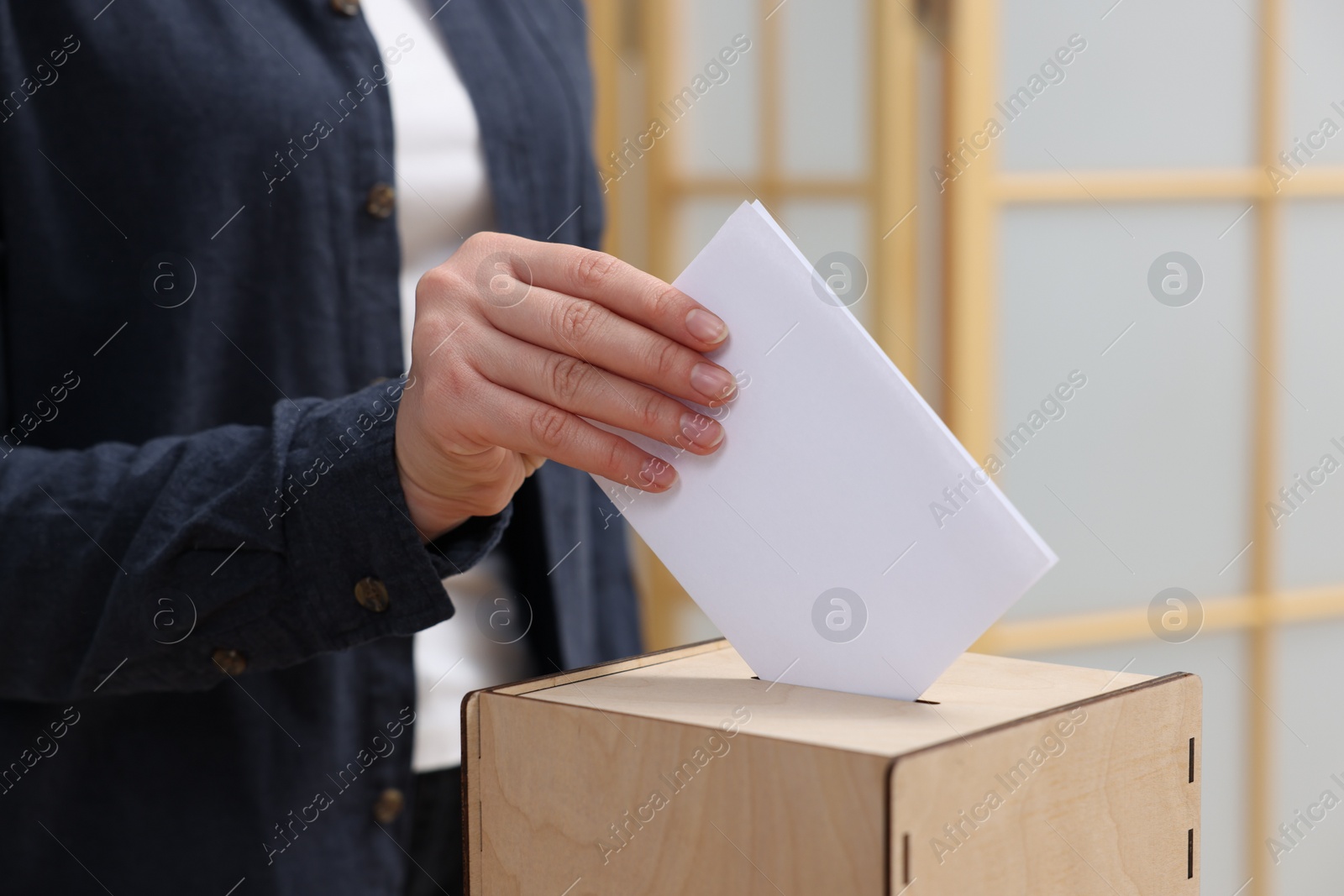 Photo of Woman putting her vote into ballot box on blurred background, closeup