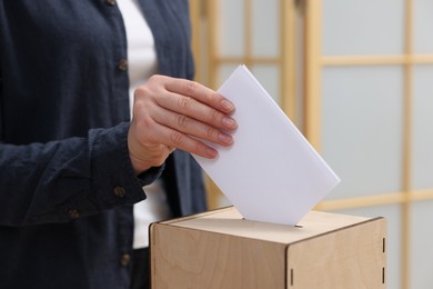 Photo of Woman putting her vote into ballot box on blurred background, closeup