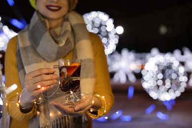 Woman with glass cup of mulled wine and garland at winter fair, closeup. Space for text