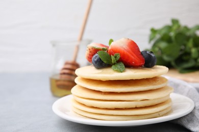 Photo of Stack of tasty pancakes with fresh berries, mint and honey on light grey table, closeup. Space for text