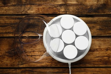 Modern yogurt maker with jars on wooden table