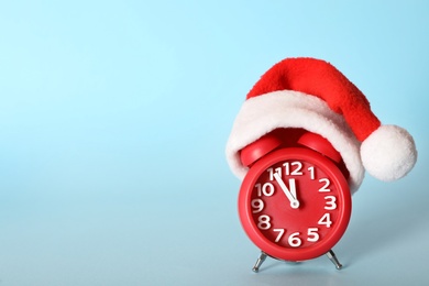 Photo of Alarm clock with Christmas decor on light blue background, space for text. New Year countdown