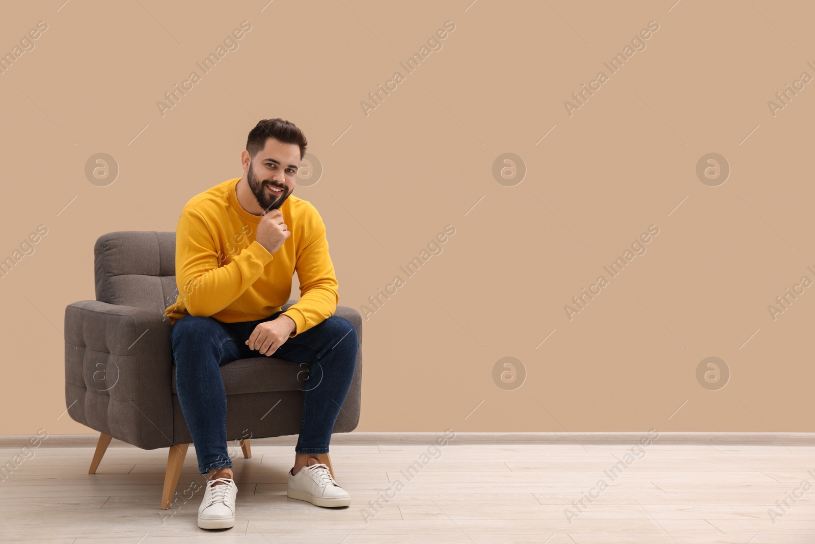 Photo of Handsome man sitting in armchair near beige wall indoors, space for text