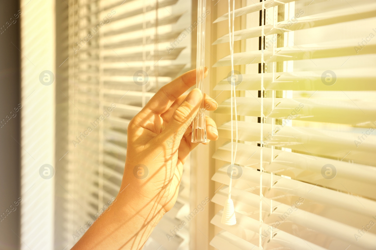 Image of Woman opening horizontal blinds on window indoors, closeup