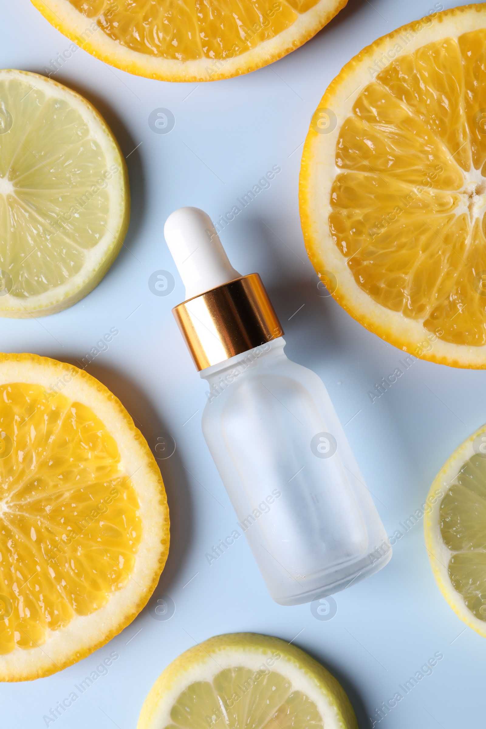 Photo of Bottle of cosmetic serum and sliced citrus fruits on light blue background, flat lay