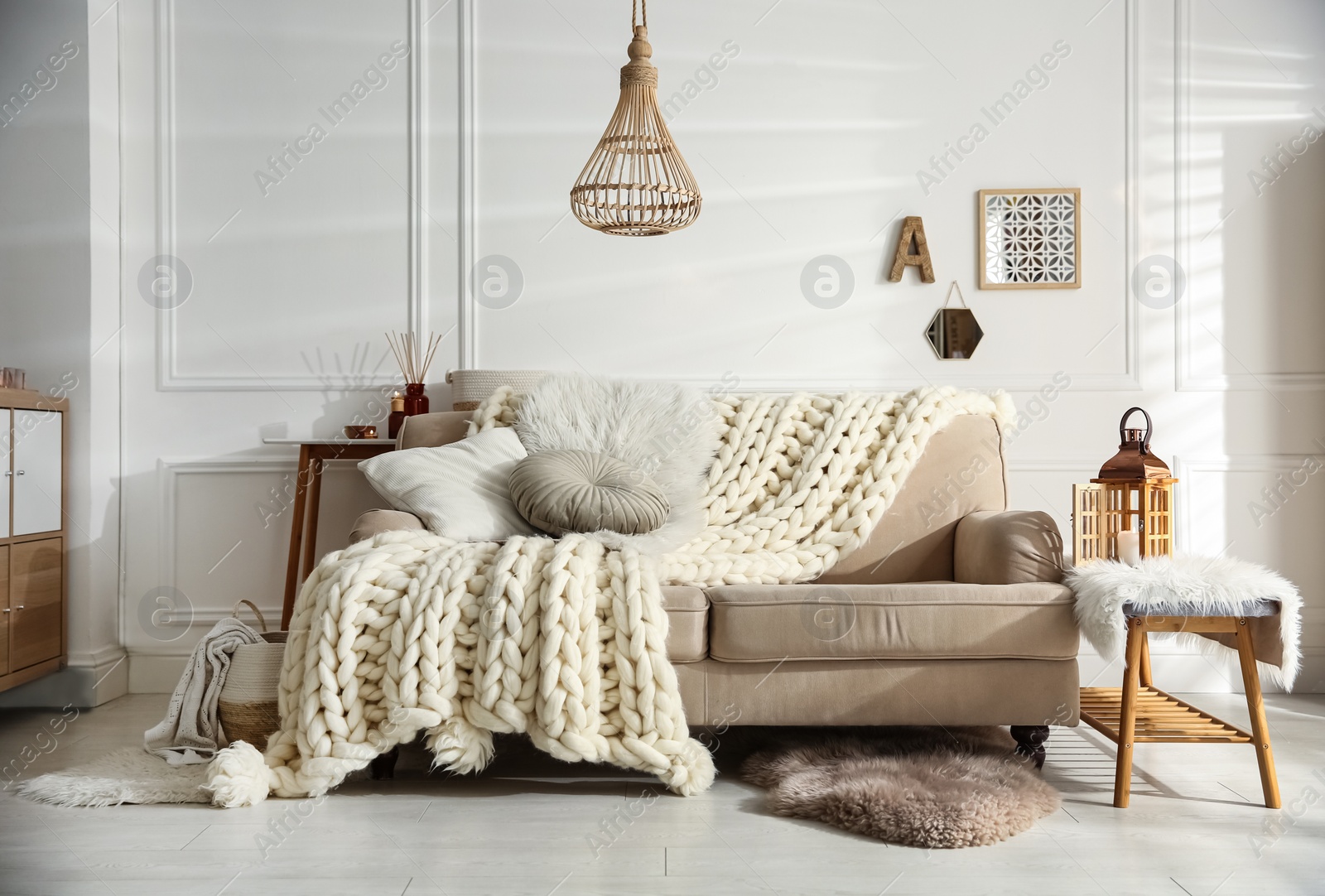 Photo of Cozy living room interior with beige sofa, knitted blanket and cushions