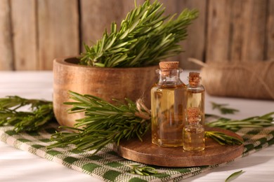 Photo of Essential oil in bottles and rosemary on white wooden table