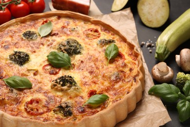 Delicious homemade vegetable quiche and products on black table, closeup