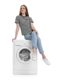 Beautiful young woman on washing machine with laundry against white background