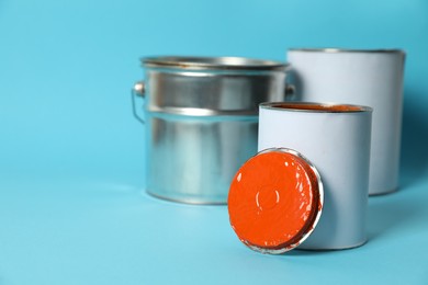 Photo of Cans and bucket of orange paint on turquoise background. Space for text