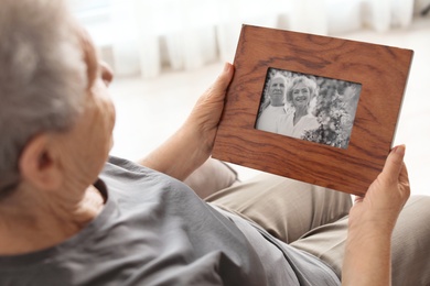 Photo of Elderly woman with framed family portrait at home