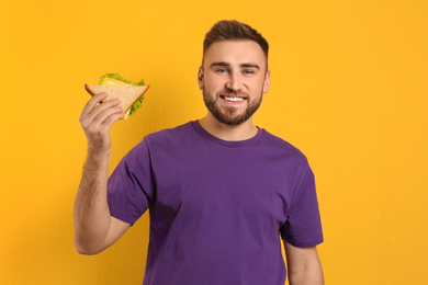 Young man with tasty sandwich on yellow background