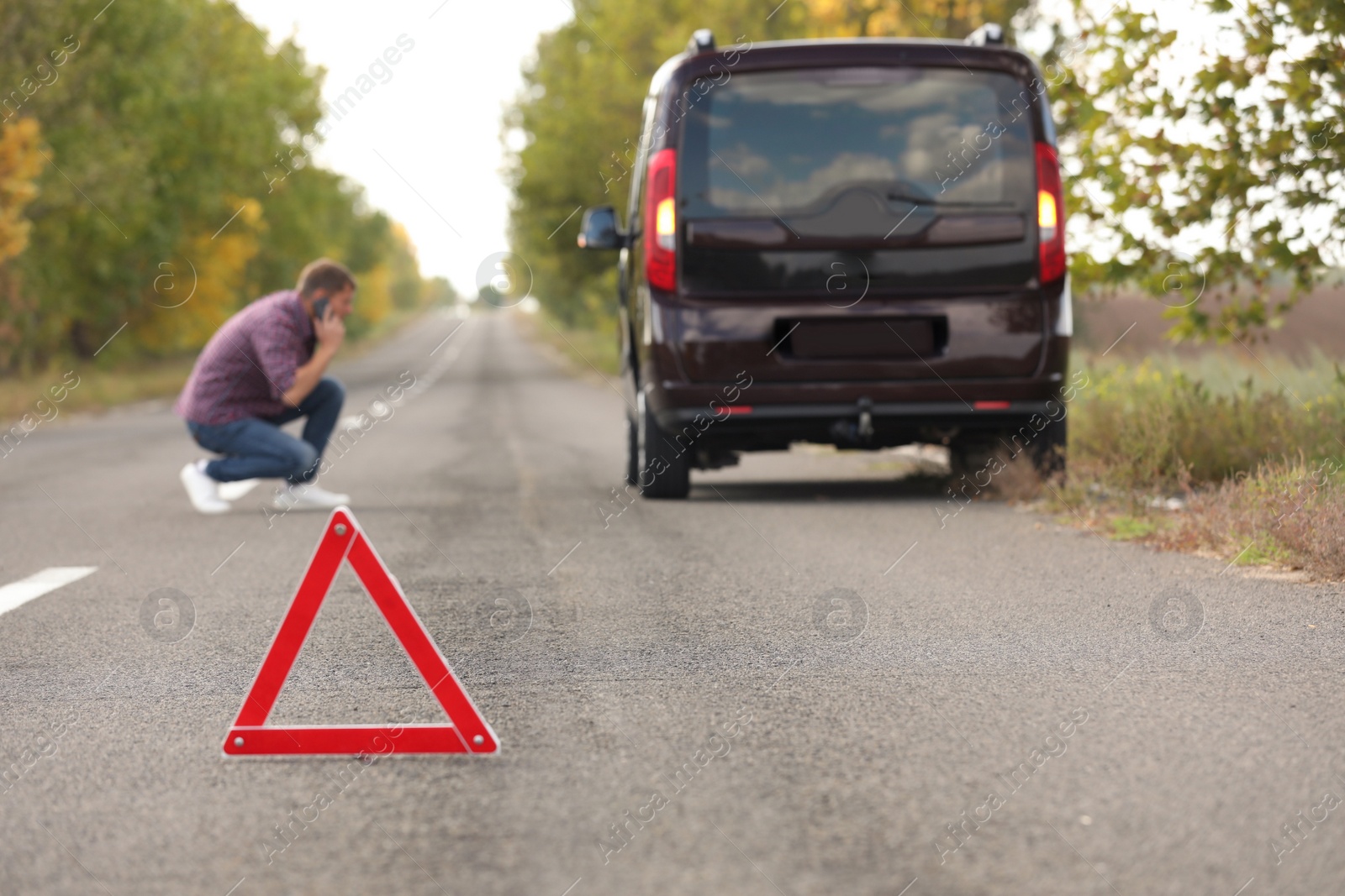 Photo of Emergency stop sign and driver near broken car on road. Auto insurance