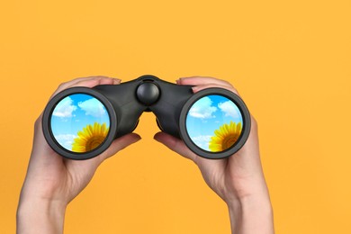 Woman holding binoculars on yellow background, closeup. Sunflower reflecting in lenses