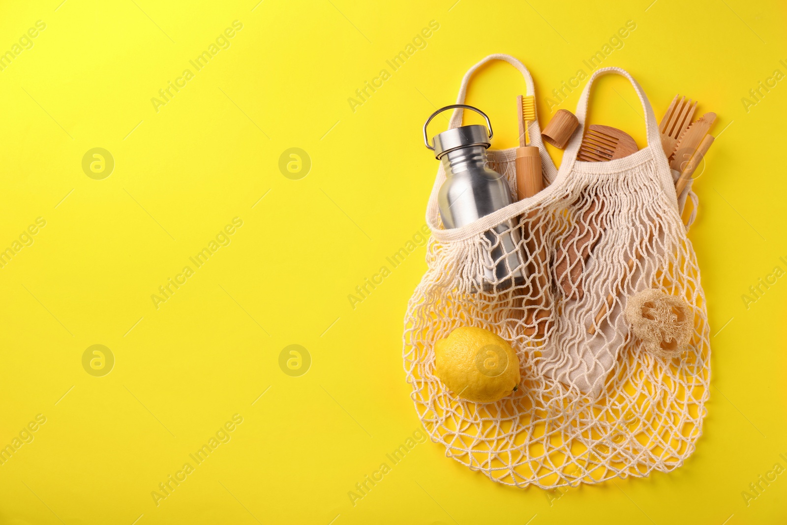 Photo of Fishnet bag with different items on yellow background, top view and space for text. Conscious consumption