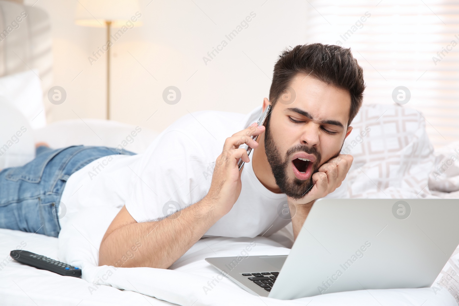 Photo of Lazy young man with laptop and smartphone on bed at home