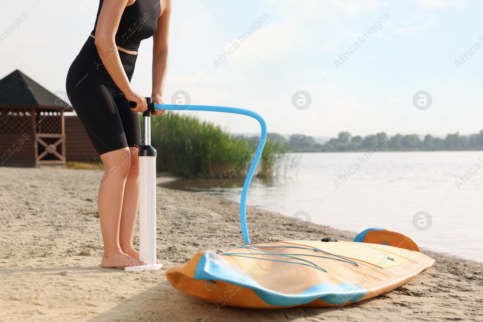 Photo of Woman pumping up SUP board on river shore, closeup