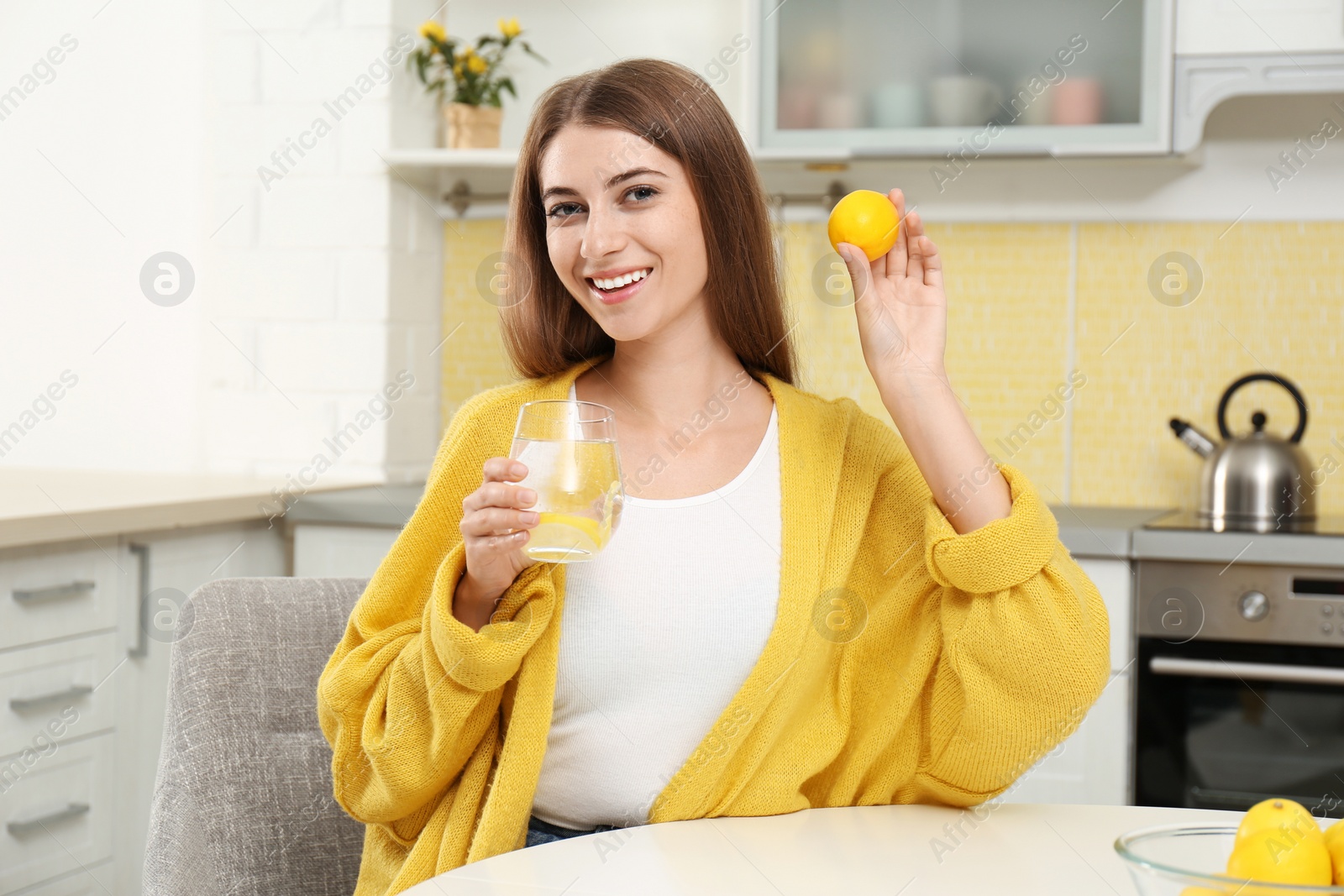 Photo of Young woman with glass of lemon water in kitchen