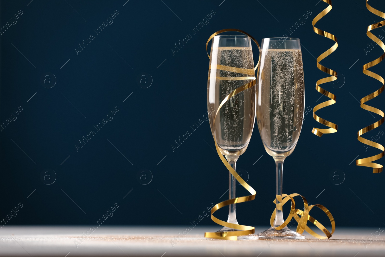 Photo of Glasses of champagne and serpentine streamers on table against dark blue background. Space for text