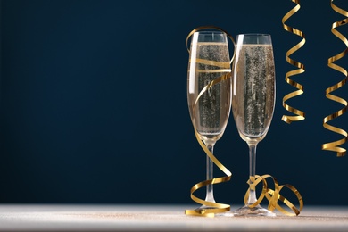 Photo of Glasses of champagne and serpentine streamers on table against dark blue background. Space for text