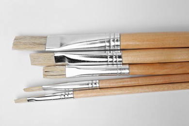 Different paint brushes on white background, top view