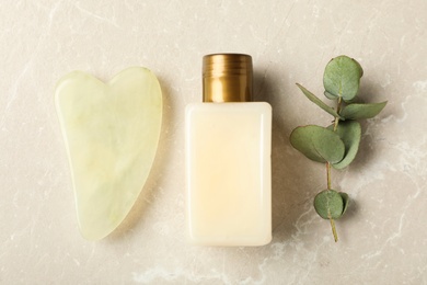 Jade gua sha tool, eucalyptus branch and cosmetic product on grey table, flat lay