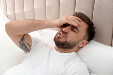 Young man suffering from migraine in bed