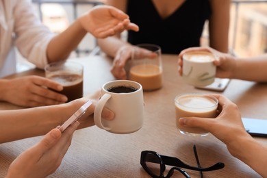 Friends drinking coffee at wooden table in cafe, closeup