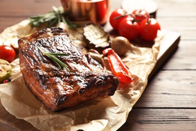 Photo of Delicious ribs served with vegetables for barbecue party on wooden table