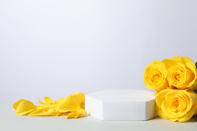 Photo of Beautiful presentation for product. Podium and yellow roses on white table, space for text