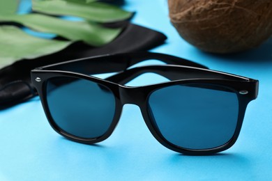 Photo of Stylish sunglasses near black cloth bag on light blue background, closeup
