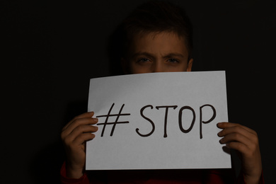 Photo of Abused little boy with hashtag STOP near black wall. Domestic violence concept